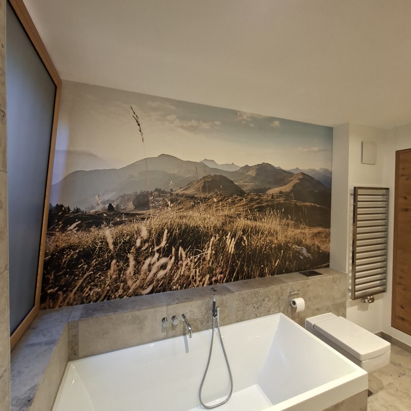 Badezimmer mit Fototapete einer Berglandschaft über der Badewanne
